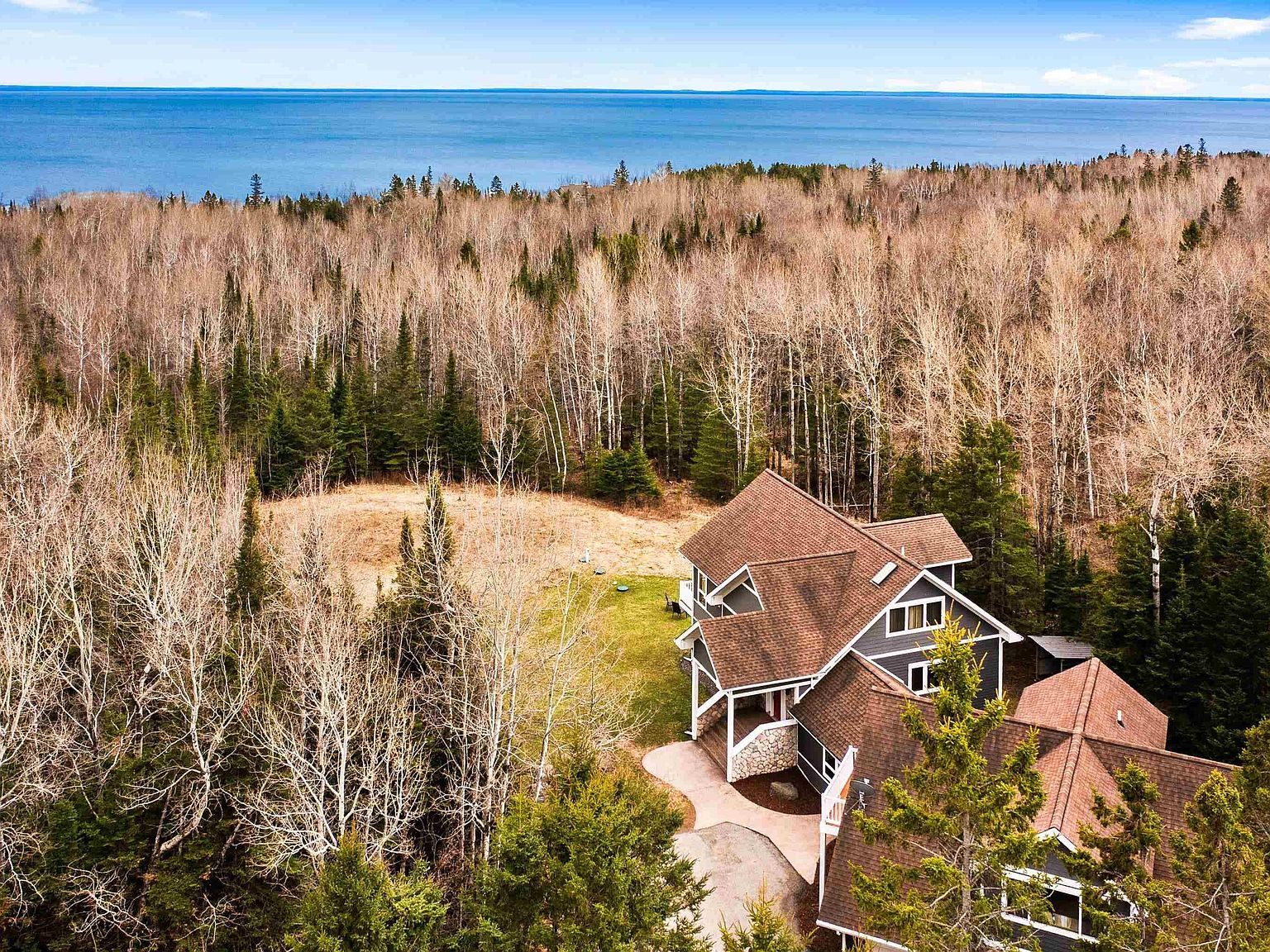Aerial view of the house in a forest clearing, with Lake Superior filling the horizon beyond the treeline